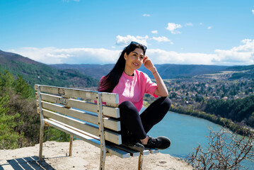 Fototapeta na wymiar Traveler woman sitting on a bench high above a blue lake with stunning view . Scenic landscape from Bulgaria