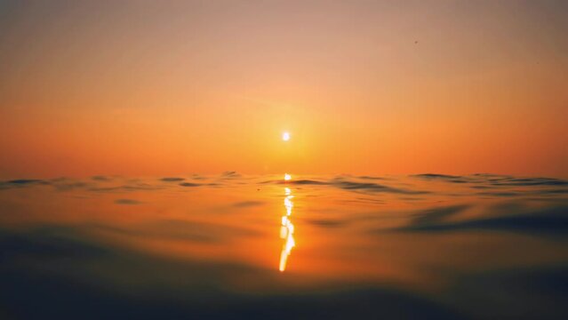 Slow Motion ocean surface from underwater at sunset with rays of light. Crystal clear breaking ocean wave with waving waterline. Sunrise over calm sea. Dawn over horizon, ocean, water - timelapse or