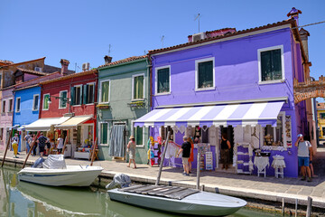 Fototapeta na wymiar Burano, Venice: Colorful houses of Burano island. Multicolored buildings on fondamenta embankment of narrow water canal with fishing boats and stone bridge, Venice Province, Veneto Region, Italy.