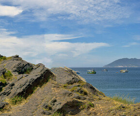 Beach at Forte São Mateus in Cabo Frio, with many rocks, the sea water around them and many mountains in the background.