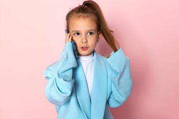 A little girl in an oversized blue blazer. Child wearing adult clothes and talking on the phone....