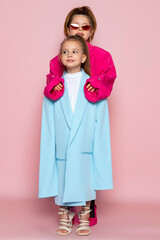 Two little girls dressed like adults. Children wearing oversized clothes. fashionable kids. Isolated on pink background.