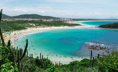 Beautiful view from above of Praia das Conchas, close to the city of Cabo Frio, with white sand beaches, blue sky, sea with clean waters and in shades of green and blue, with mountains in the backgrou