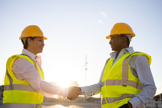 Female engineers in site waistcoats shaking hands on street