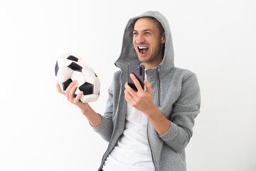 Shocked young man football fan cheer up support favorite team with soccer ball using mobile cell phone People sport leisure lifestyle concept