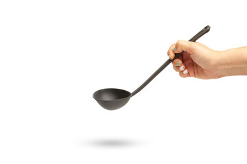 Mano de mujer sosteniendo un cucharón de cocina de plástico negro sobre un fondo blanco liso y...