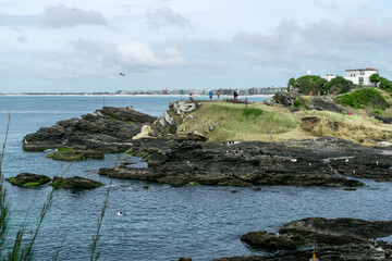 Praia do Forte, with the fort on top of the hill, sea, large rocks, cloudy sky and the city in the background.
