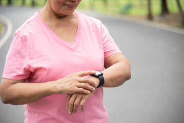 Close up Asian senior woman hands checking his heartbeat with smart watch at nature park. Mature...