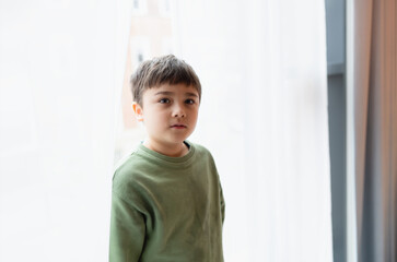 Portrait Kid boy with smiling face looking up standing behind lace curtain with bright light in morning,Positive children concept