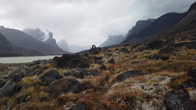 Stone inukshuk in the remote arctic wilderness of Baffin Island, Nunavut, Canada. Akshayuk pass hike in Auyuittuq national park. Cloudy day of arctic autumn.