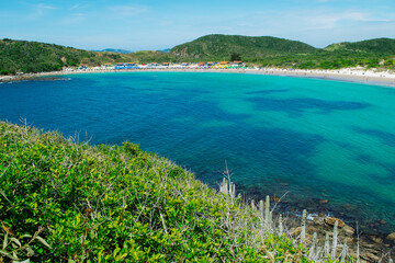 Top view of the beautiful beach of Conchas, close to the city of Cabo Frio, with white sand beaches, blue sky, sea with clean waters and in shades of green and blue, with mountains in the background.