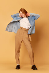 Fototapeta premium One young positive, pretty girl, student wearing casual clothes posing and smiling at camera over ginger background. Happiness, joyful