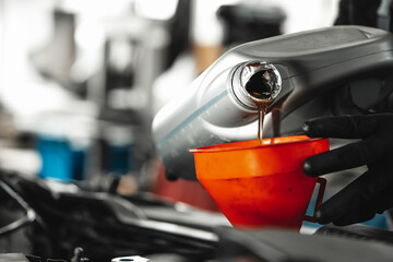 Obraz premium Close up of car service worker pouring new oil into car engine