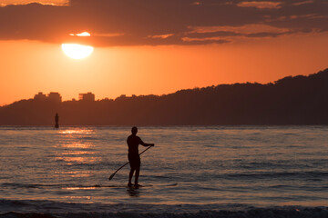 Fototapeta na wymiar Silhouette of man practicing stand up paddle in the bay of santos city at sunset.