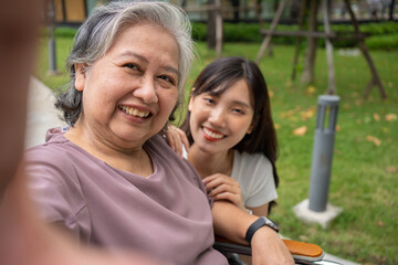 Naklejka premium Happy Asian patients in a wheelchair use smartphones to take pictures with careful caregivers or nurse Concept of happy retirement with care from a caregiver and Savings and senior health insurance.