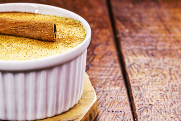 Bowl with corn jam called Curau, jimbelê or hominy, decorated with cinnamon bark in cinnamon powder, rural background, copyspace, typical food of the June festivities