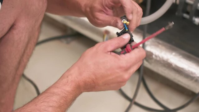 Electrician connects cables to device, males hands worker