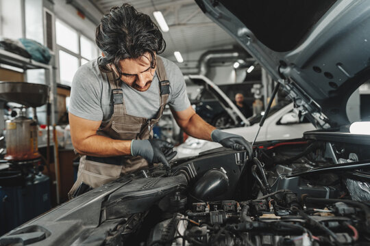 Young male mechanic examining engine under hood of car at the repair garage