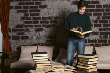 A hard learning student dressed neatly, in round glasses is reading and studying among piles and...
