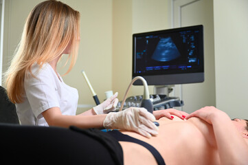 Professional female gynecologist performs an examination of the mammary glands using ultrasound...