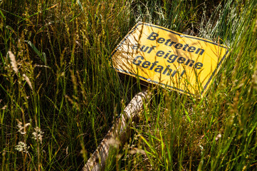 Schild Betreten auf eigene Gefahr liegt im hohen Gras