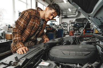 Young male mechanic examining engine under hood of car at the repair garage