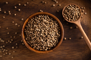 Uncooked coriander seeds bowl. Studio shoot isolated on rustic background. Coriander seeds spread on dark background. Up view shoot.