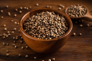 Uncooked coriander seeds bowl. Studio shoot isolated on rustic background. Coriander seeds spread on dark background. 45 degree shoot.