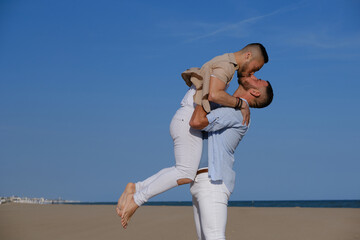 Man holding up his boyfriend and kissing while enjoying a sunny day at the beach.