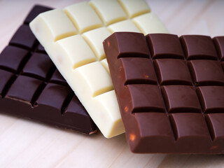 A closeup short of three chocolate bars - milk chocolate, dark chocolate and white chocolate on a wooden background.