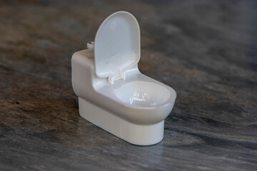 A white plastic toy toilet stands on a marble surface