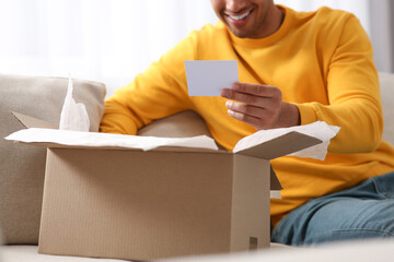 Young man holding greeting card near parcel with Christmas gift, closeup