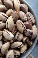 Bowl with pistachios on a grey concrete background. Green salted pistachios in ceramic bowl. Copy space, top view.