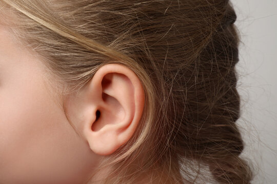 Closeup view of little girl against light gray background, focus on ear
