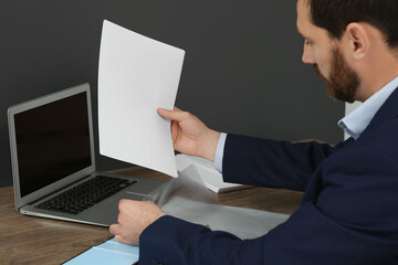 Businessman putting document into punched pocket at wooden table in office, closeup