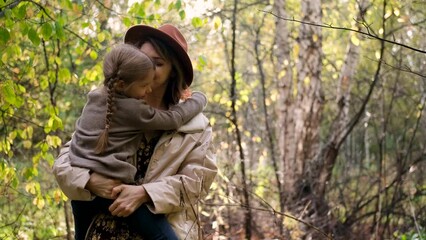 Hello September. A young mother in a brown hat and a little daughter walk in the city park in autumn. Mom holds the girl in her arms and hugs her tightly with love.
