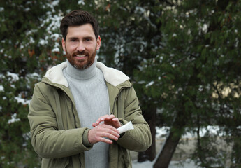 Fototapeta premium Man applying cream from tube onto hand outdoors, space for text. Winter care