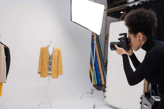 side view of african american content maker with digital camera taking picture of trendy jacket in photo studio.