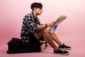 A lost young traveller or tourist sitting on a baggage or spinner luggage and looking at the map.