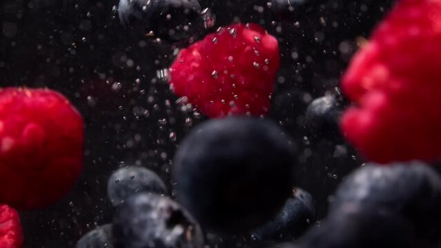 Raspberries and blueberries fall into the water. Underwater video shooting. Close up shot