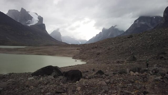 Male hiker with very big and heavy backpack walking around summit lake in the remote arctic wilderness of Baffin Island, Nunavut, Canada. Akshayuk pass hike in Auyuittuq national park.