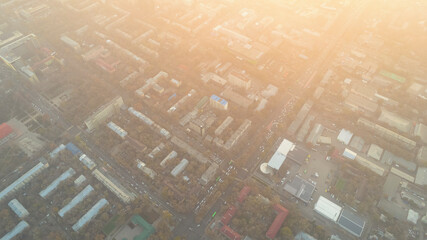 Epic gray smog is visible at sunset over the city. Aerial view from the drone of houses, roads, cars and parks. White clouds are illuminated by orange rays of the sun. The city is suffocating. Almaty