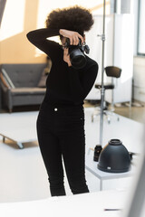 african american content producer in black clothes taking picture on professional digital camera while working in photo studio.
