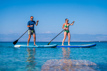 Couple riding SUP stand up paddle on vacation.