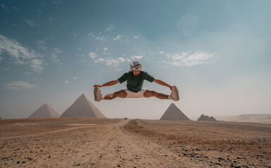 young man with a turban jumps in the desert with the pyramids in the background. Cairo. Egypt
