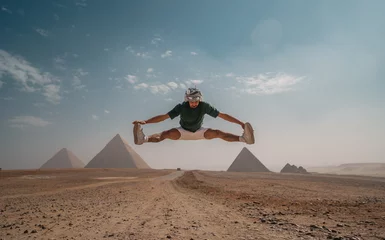 Papier Peint photo Cappuccino young man with a turban jumps in the desert with the pyramids in the background. Cairo. Egypt
