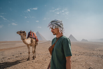 young man in a turban next to a camel with the pyramids in the background. El Cairo. Egypt