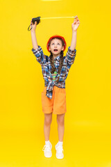 A little girl in an orange construction helmet holds a measuring tape. The concept of renovation in the children's room. The child is an engineer. Vertical. Full height. Yellow isolated background.