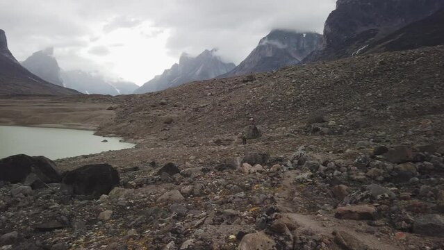 Male hiker with very big and heavy backpack walking around summit lake in the remote arctic wilderness of Baffin Island, Nunavut, Canada. Akshayuk pass hike in Auyuittuq national park.