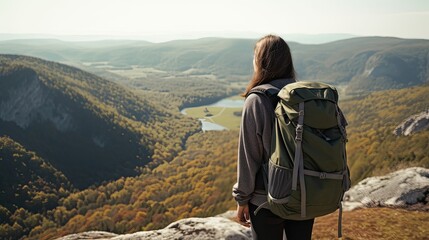 Person with a backpack standing on a cliff, overlooking a river and autumn forest.